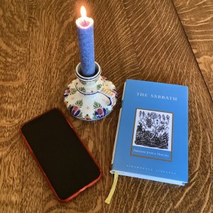 Candle, book titled The Sabbath, and iphone