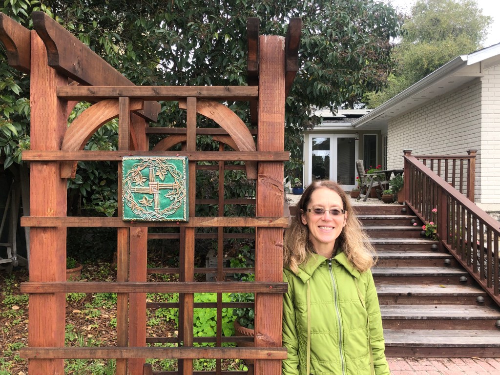 Author standing next to the bare wooden garden arch where the plaque is hung